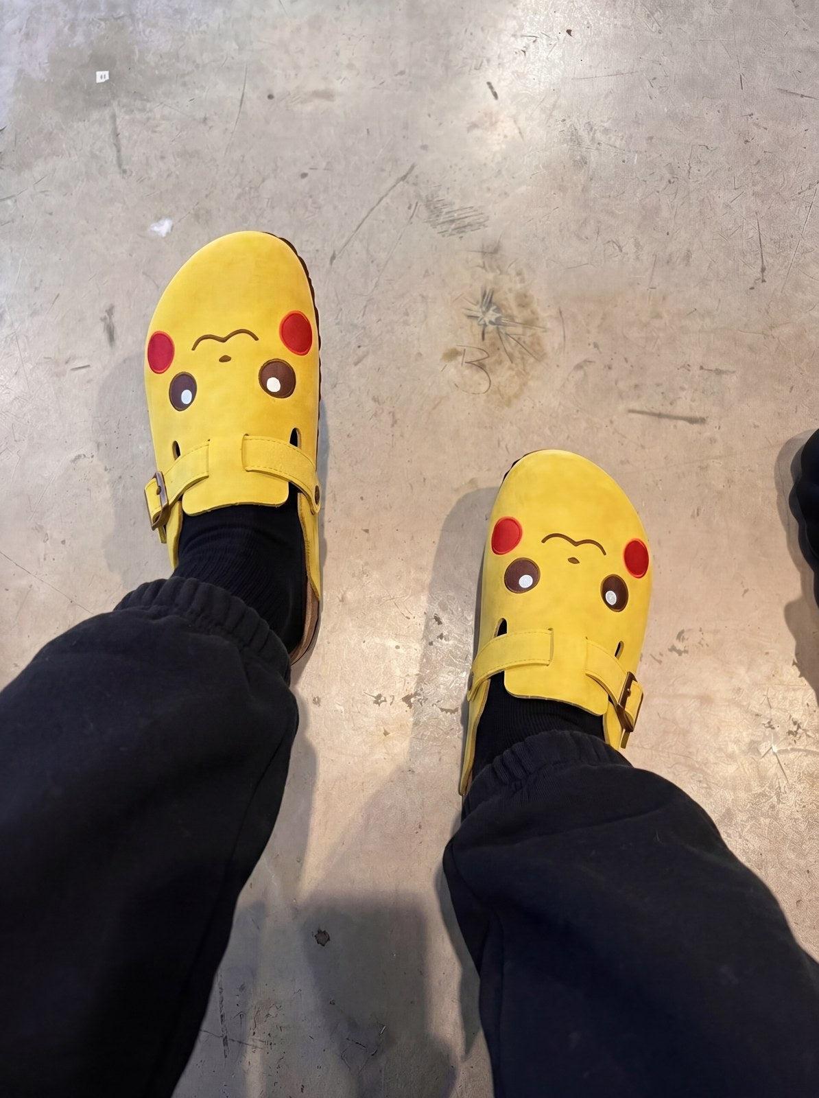Pikachu clogs worn with black sweatpants, indoor