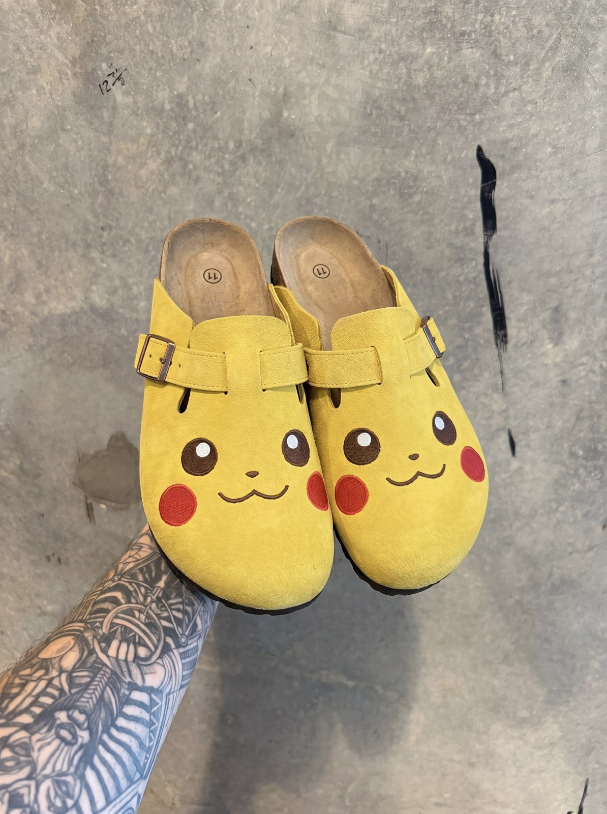 Pikachu clogs pair held up against concrete wall